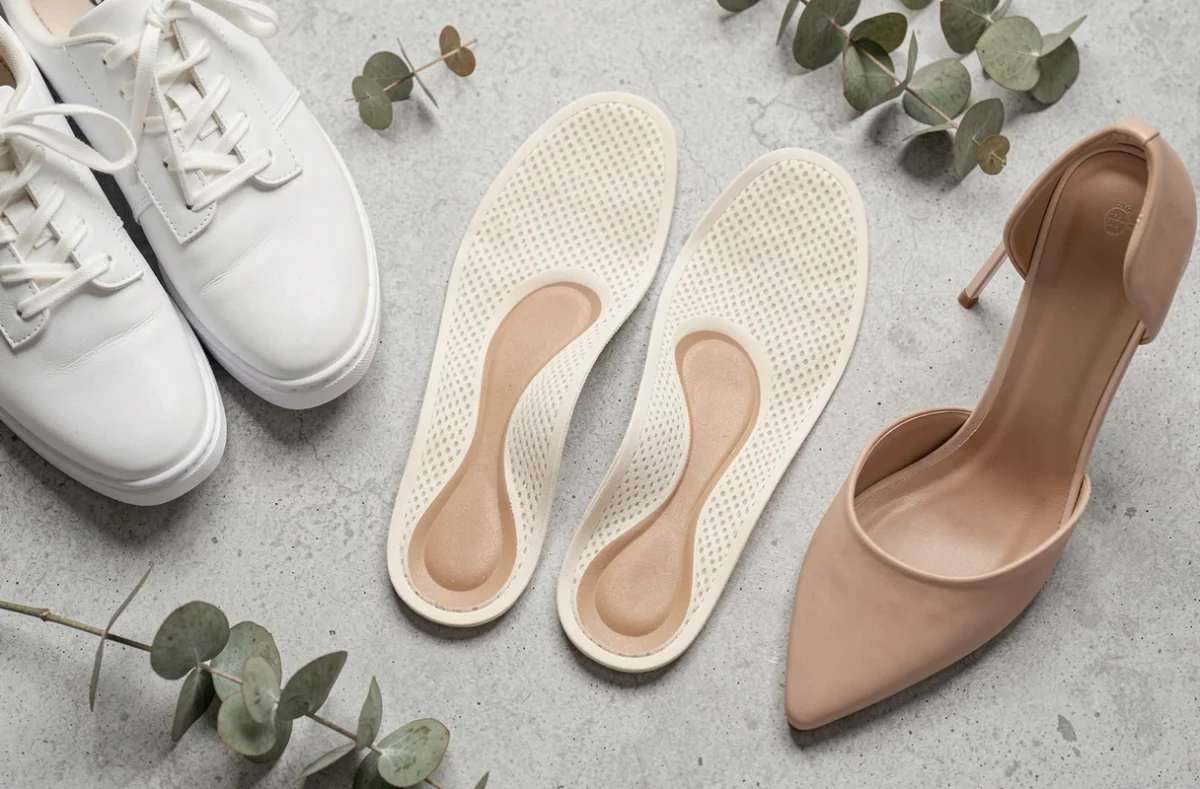 Vue à plat de semelles orthopédiques pour pieds plats posées à côté de chaussures féminines élégantes sur fond béton